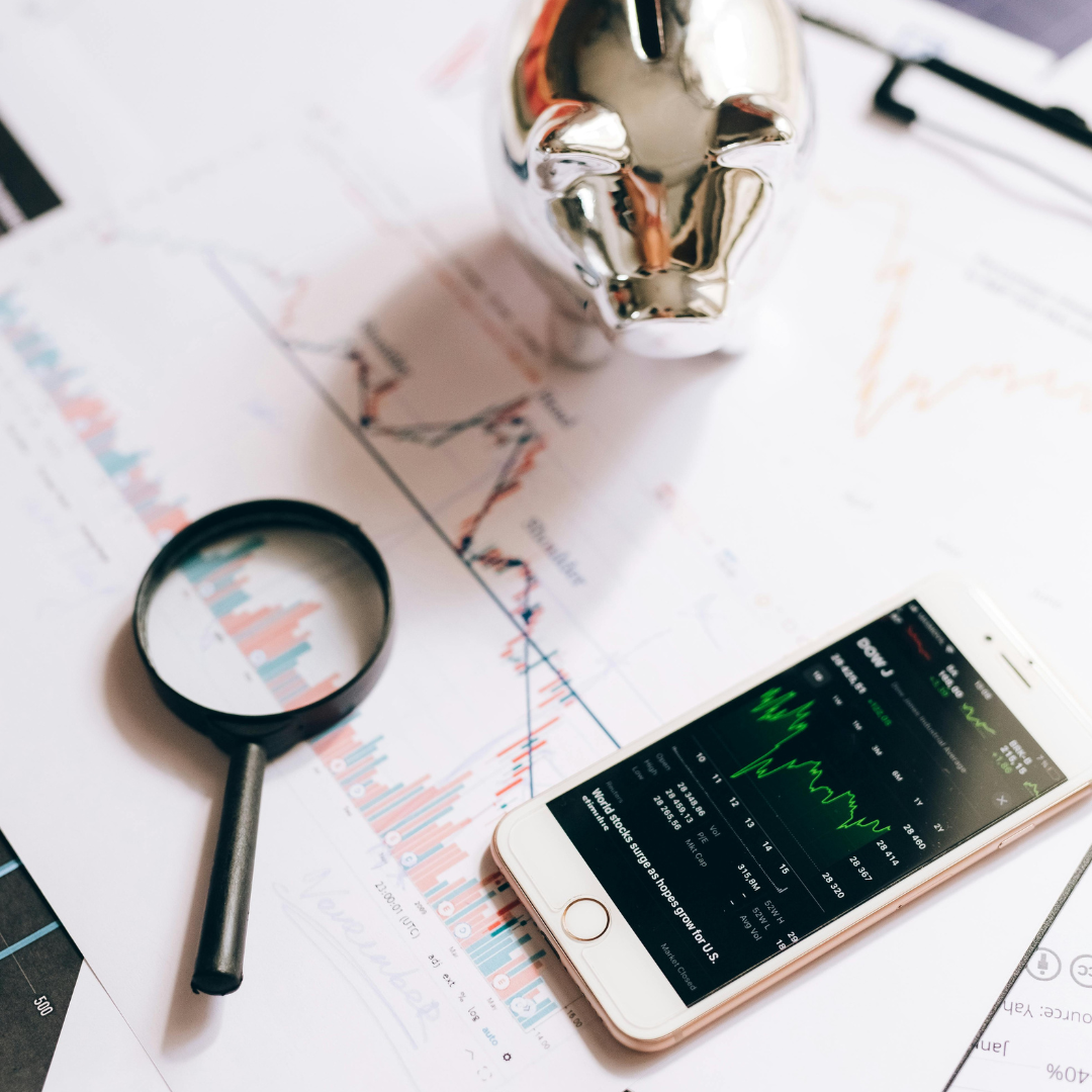 A phone, a piggy bank, and a magnifying glass sit on a desk. 